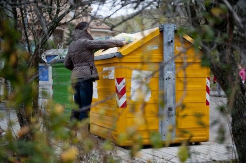 Una mujer deposita una bolsa en el contenedor amarillo. 