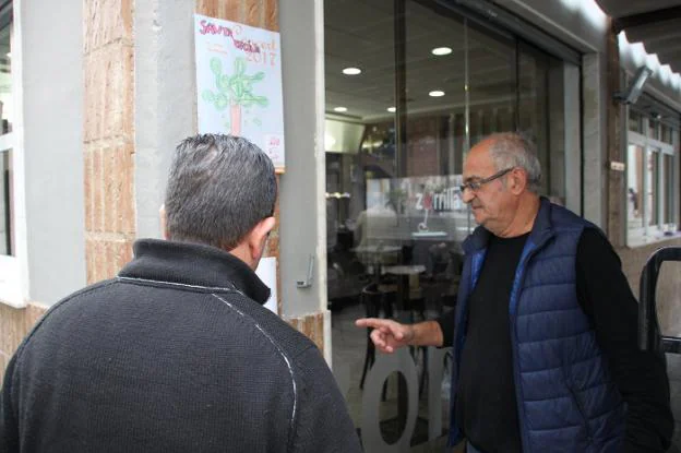 Dos vecinos de Pego observan una esquela colgada junto a otros carteles en la fachada de uno de los bares del municipio. 