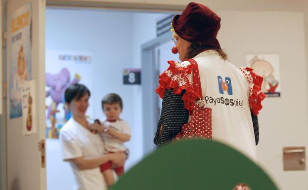 Un niño, en brazos de una enfermera, mira a una de las voluntarias de PayaSOSpital en el Hospital Peset.