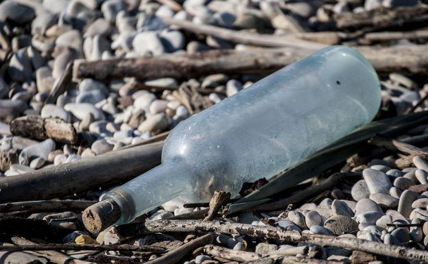 Una botella tirada en una playa de piedas.