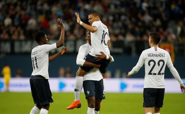 Pogba sostiene en brazos a Mbappé, que choca la mano con Dembélé. 