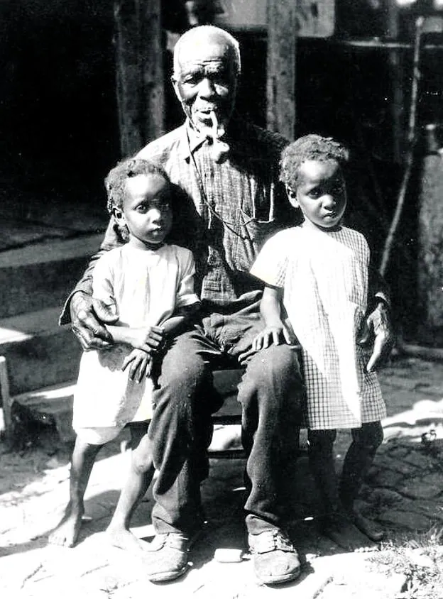 Las imágenes.  Zora Neale Hurston obtuvo las únicas fotos que se conservan de Cudjo Lewis. Arriba, con dos tataranietas. A la derecha, en su casa de Africatown, en Alabama. 