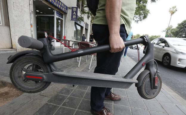 Un usuario lleva su patinete plegado por una calle de Valencia. 