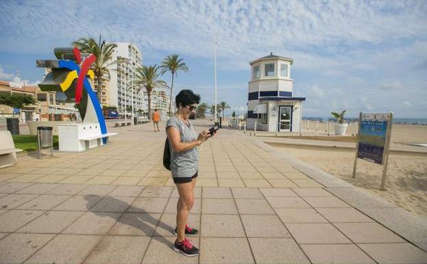 Una mujer comprueba el teléfono móvil en el paseo marítimo de Gandia junto al punto de recarga. 