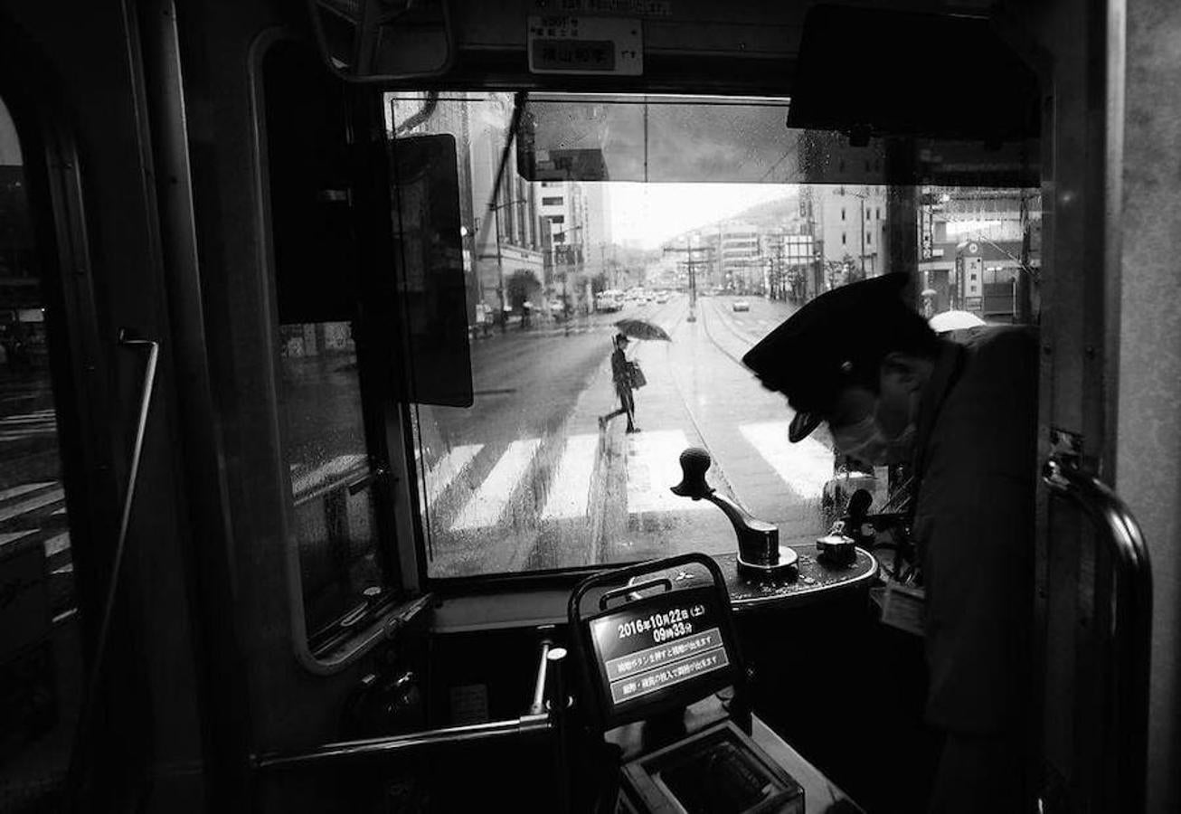 Un día corriente en la principal calle de Nagasaki ha conseguido el primer premio de la categoría Ciudades. La imagen tomada un día lluvioso desde el tranvía es un intento de mostrar el paisaje urbano desde el interior del transporte. Además, represente un buen contraste a la imagen que se tiene del caos de los centros urbanos de Japón y de la antigüedad del tranvía. 