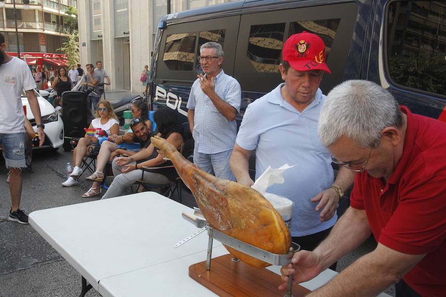 La huelga indefinida de taxistas en Valencia tiene como epicentro la calle Colón de Valencia. Allí, decenas de vehículo blancos están aparcados mientras los conductores tienen puesta toda la atención en la sede de Delegación del Gobierno. El único carril abierto es por el que circulan los autobuses de la EMT ante los taxistas que sentados en sillas plegables comentan, protestan y hace sonar el claxon. Unos conductores comparten café ante una mesa, mientras otros se muestran nerviosos con un cigarro en la mano. Ante la hora de comer, panes para los presenten y hasta se ha empezado un jamón entero. Las botellas de agua no han faltado ante las altas temperaturas que se registran en el centro de la ciudad.