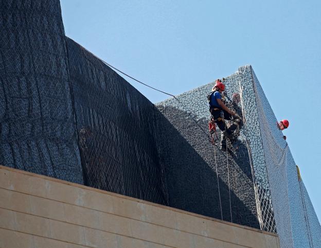 Varios técnicos colocan una malla en la fachada del Palau para evitar más desprendimientos. 