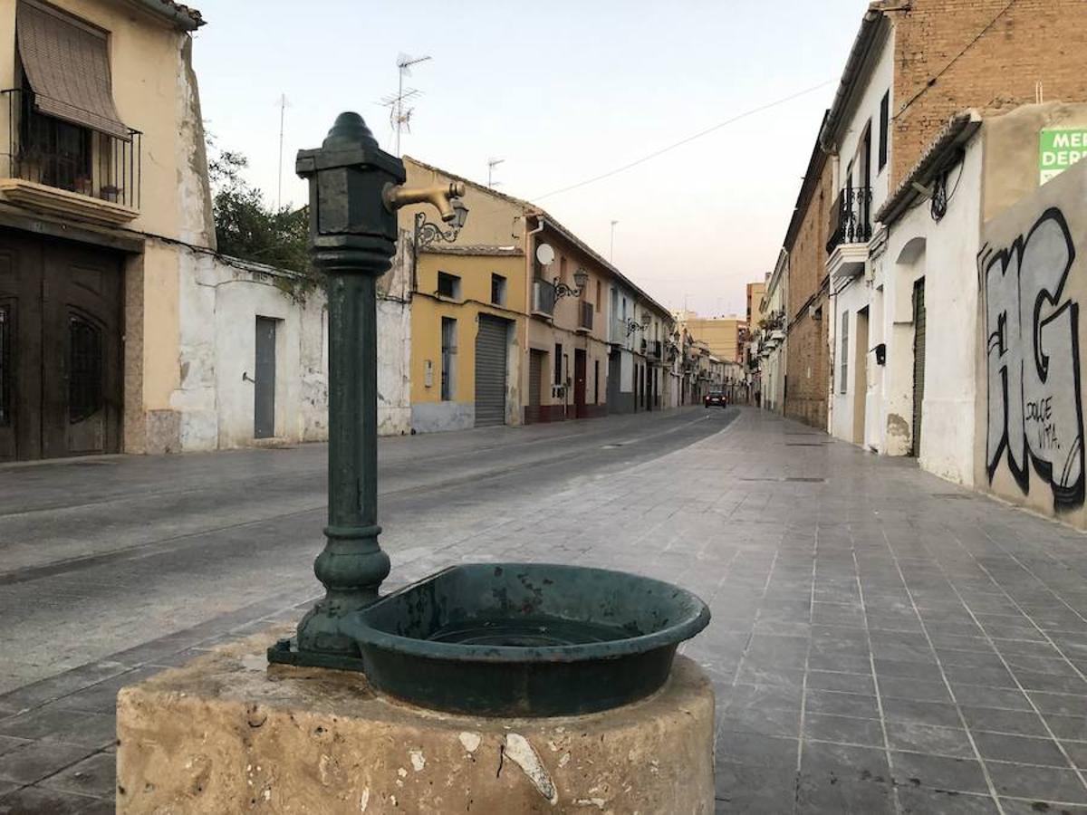 Es una de esas zonas poco conocidas de Valencia. El barrio de Campanar reúne todas esas características que se espera encontrar en un remoto y solitario pueblo, y no en plena urbe. Calles tranquilas, casas antiguas, fachadas con un encanto diseñado por el paso del tiempo. Recorrer sus aceras es pasear por un rincón de paz, ajeno al constante ajetreo de la ciudad. Una especie de paréntesis entre el tráfico, ruido y bullicio, en un lugar donde el reloj parece detenerse, mientras las sombras del atardecer se van colando por cada resquicio. Entre paredes blancas, tonalidades ocre, fuentes y ventanas que se asoman a décadas de historia, permanecen mosaicos en honor a lo que el pueblo fue. Azulejos que recuerdan al oficio hornero y la patrona, la Virgen de Campanar, cuelgan de paredes en las que los ladrillos soportan más años que peso. Casas, unas bajas y otras ilustres, que recuerdan un tiempo no tan lejano, muestras de la Valencia pasada rodeadas de la ciudad actual. 