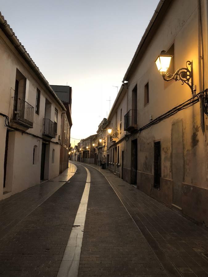 Es una de esas zonas poco conocidas de Valencia. El barrio de Campanar reúne todas esas características que se espera encontrar en un remoto y solitario pueblo, y no en plena urbe. Calles tranquilas, casas antiguas, fachadas con un encanto diseñado por el paso del tiempo. Recorrer sus aceras es pasear por un rincón de paz, ajeno al constante ajetreo de la ciudad. Una especie de paréntesis entre el tráfico, ruido y bullicio, en un lugar donde el reloj parece detenerse, mientras las sombras del atardecer se van colando por cada resquicio. Entre paredes blancas, tonalidades ocre, fuentes y ventanas que se asoman a décadas de historia, permanecen mosaicos en honor a lo que el pueblo fue. Azulejos que recuerdan al oficio hornero y la patrona, la Virgen de Campanar, cuelgan de paredes en las que los ladrillos soportan más años que peso. Casas, unas bajas y otras ilustres, que recuerdan un tiempo no tan lejano, muestras de la Valencia pasada rodeadas de la ciudad actual. 