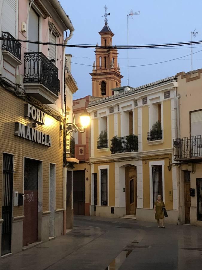 Es una de esas zonas poco conocidas de Valencia. El barrio de Campanar reúne todas esas características que se espera encontrar en un remoto y solitario pueblo, y no en plena urbe. Calles tranquilas, casas antiguas, fachadas con un encanto diseñado por el paso del tiempo. Recorrer sus aceras es pasear por un rincón de paz, ajeno al constante ajetreo de la ciudad. Una especie de paréntesis entre el tráfico, ruido y bullicio, en un lugar donde el reloj parece detenerse, mientras las sombras del atardecer se van colando por cada resquicio. Entre paredes blancas, tonalidades ocre, fuentes y ventanas que se asoman a décadas de historia, permanecen mosaicos en honor a lo que el pueblo fue. Azulejos que recuerdan al oficio hornero y la patrona, la Virgen de Campanar, cuelgan de paredes en las que los ladrillos soportan más años que peso. Casas, unas bajas y otras ilustres, que recuerdan un tiempo no tan lejano, muestras de la Valencia pasada rodeadas de la ciudad actual. 