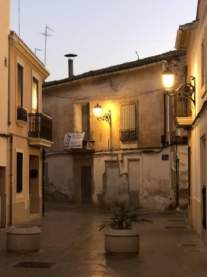 Es una de esas zonas poco conocidas de Valencia. El barrio de Campanar reúne todas esas características que se espera encontrar en un remoto y solitario pueblo, y no en plena urbe. Calles tranquilas, casas antiguas, fachadas con un encanto diseñado por el paso del tiempo. Recorrer sus aceras es pasear por un rincón de paz, ajeno al constante ajetreo de la ciudad. Una especie de paréntesis entre el tráfico, ruido y bullicio, en un lugar donde el reloj parece detenerse, mientras las sombras del atardecer se van colando por cada resquicio. Entre paredes blancas, tonalidades ocre, fuentes y ventanas que se asoman a décadas de historia, permanecen mosaicos en honor a lo que el pueblo fue. Azulejos que recuerdan al oficio hornero y la patrona, la Virgen de Campanar, cuelgan de paredes en las que los ladrillos soportan más años que peso. Casas, unas bajas y otras ilustres, que recuerdan un tiempo no tan lejano, muestras de la Valencia pasada rodeadas de la ciudad actual. 