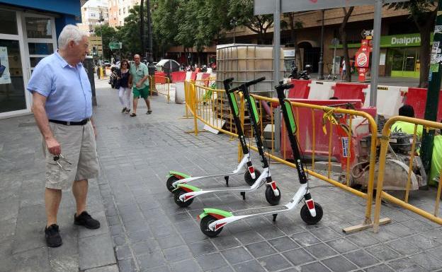 Un viandante observa tres unidades de los patinetes eléctricos repartidos por Valencia esta semana.