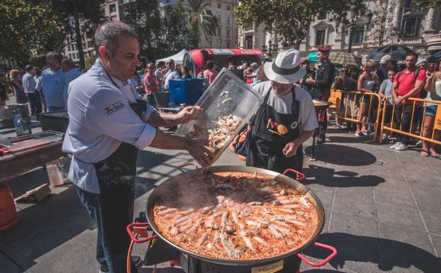 Una pareja de cocineros echa el arroz a la paella durante la celebración del Día Mundial de la Paella.