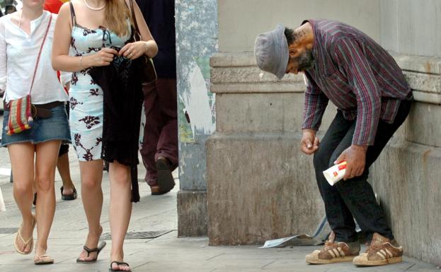 Varias personas pasan junto a un mendigo en Barcelona. 