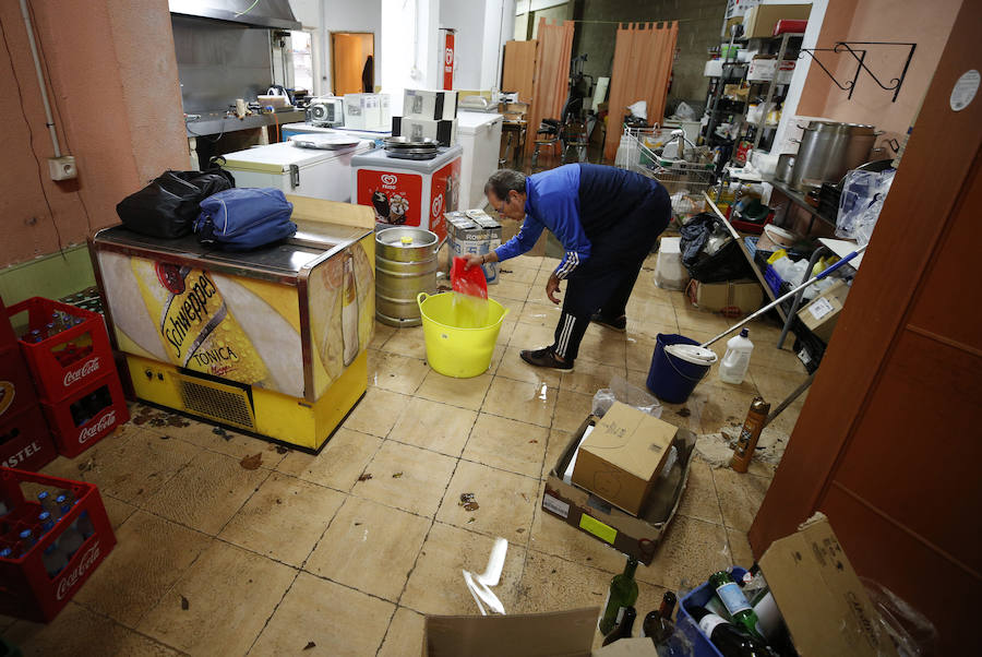 Un vecino achica agua de su local tras la gota fría.