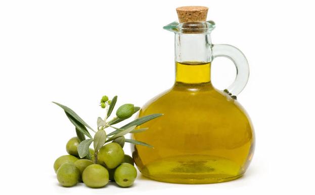 Un racimo de olivas junto a una jarra de aceite de oliva.