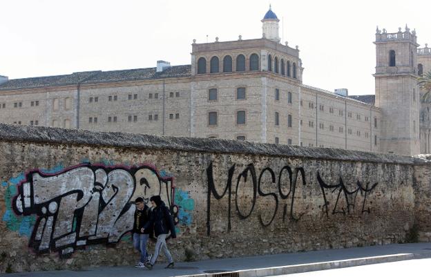 Dos jóvenes pasan junto a una de las pintadas del muro que cierra la huerta de la actual Biblioteca Valenciana. 