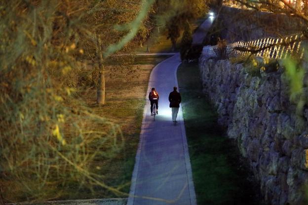 Un ciclista y un peatón se cruzan en el tramo poco iluminado del carril bici del viejo cauce. 