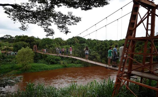 Gente camina en puente sobre el río desbordado. 