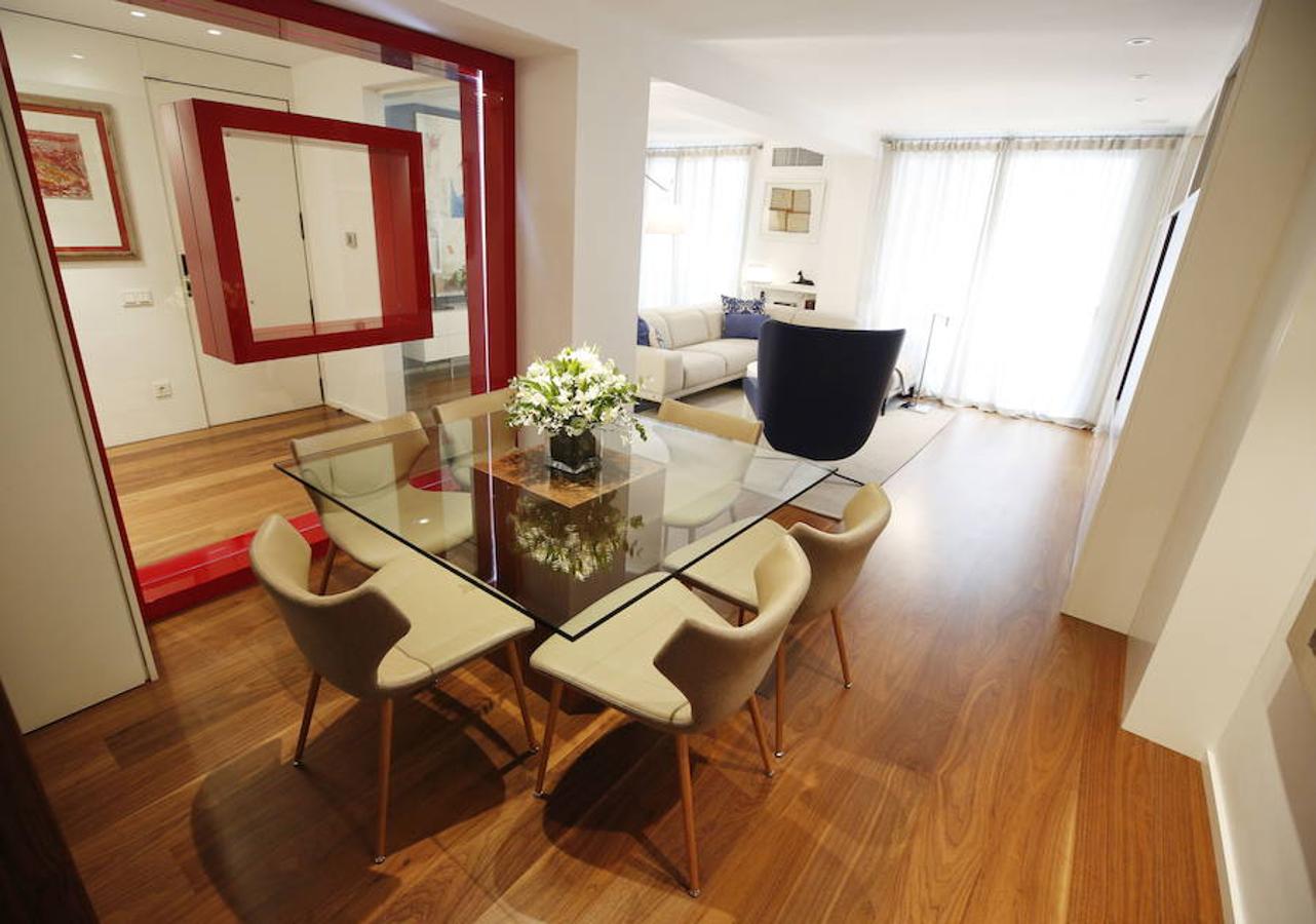 Las peticiones que Mariche Correcher planteó a la diseñadora creativa Carmen Bayarri estaban muy claras: que la casa tuviera muchos armarios, que la cocina y el salón estuviesen unidos pero a la vez se pudieran independizar y que la zona más tranquila de la casa albergara una suerte de suite en la que poder refugiarse después de la jornada de trabajo. Además le pidió que al entrar a la vivienda pudiera ver un ramo de flores. Con estas premisas, hace cuatro años se esbozó el proyecto en esta casa ubicada en una finca con carácter en pleno Ensanche valenciano. Para vestir el suelo escogieron madera de nogal, al igual que en las puertas que dividen las estancias. El resto de las puertas son blancas con las manivelas en negro y van de suelo a techo buscando potenciar la sensación de amplitud. En los baños instalaron porcelánico negro en el suelo que contrasta muy bien con el nogal. Carmen propuso ubicar junto a la entrada una escultura lacada flotante en rojo Ferrari que enmarca el espacio y permite ver el ramo de flores que reposa sobre la mesa del salón nada más entrar, que era uno de los deseos de la propietaria. La iluminación está integrada en la propia arquitectura. En lugar de obviar los pilares se decidió marcarlos de manera interna con filas de luz para ofrecer un ambiente casi escultórico. 