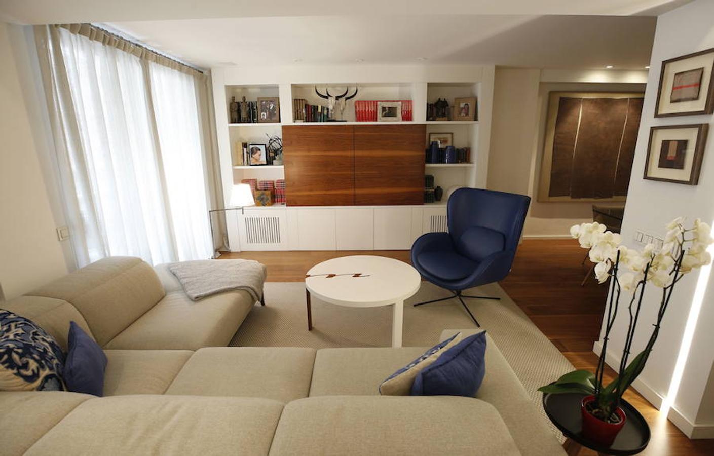 Las peticiones que Mariche Correcher planteó a la diseñadora creativa Carmen Bayarri estaban muy claras: que la casa tuviera muchos armarios, que la cocina y el salón estuviesen unidos pero a la vez se pudieran independizar y que la zona más tranquila de la casa albergara una suerte de suite en la que poder refugiarse después de la jornada de trabajo. Además le pidió que al entrar a la vivienda pudiera ver un ramo de flores. Con estas premisas, hace cuatro años se esbozó el proyecto en esta casa ubicada en una finca con carácter en pleno Ensanche valenciano. Para vestir el suelo escogieron madera de nogal, al igual que en las puertas que dividen las estancias. El resto de las puertas son blancas con las manivelas en negro y van de suelo a techo buscando potenciar la sensación de amplitud. En los baños instalaron porcelánico negro en el suelo que contrasta muy bien con el nogal. Carmen propuso ubicar junto a la entrada una escultura lacada flotante en rojo Ferrari que enmarca el espacio y permite ver el ramo de flores que reposa sobre la mesa del salón nada más entrar, que era uno de los deseos de la propietaria. La iluminación está integrada en la propia arquitectura. En lugar de obviar los pilares se decidió marcarlos de manera interna con filas de luz para ofrecer un ambiente casi escultórico. 