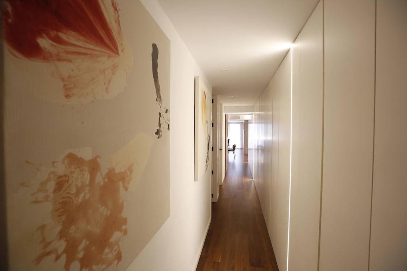 Las peticiones que Mariche Correcher planteó a la diseñadora creativa Carmen Bayarri estaban muy claras: que la casa tuviera muchos armarios, que la cocina y el salón estuviesen unidos pero a la vez se pudieran independizar y que la zona más tranquila de la casa albergara una suerte de suite en la que poder refugiarse después de la jornada de trabajo. Además le pidió que al entrar a la vivienda pudiera ver un ramo de flores. Con estas premisas, hace cuatro años se esbozó el proyecto en esta casa ubicada en una finca con carácter en pleno Ensanche valenciano. Para vestir el suelo escogieron madera de nogal, al igual que en las puertas que dividen las estancias. El resto de las puertas son blancas con las manivelas en negro y van de suelo a techo buscando potenciar la sensación de amplitud. En los baños instalaron porcelánico negro en el suelo que contrasta muy bien con el nogal. Carmen propuso ubicar junto a la entrada una escultura lacada flotante en rojo Ferrari que enmarca el espacio y permite ver el ramo de flores que reposa sobre la mesa del salón nada más entrar, que era uno de los deseos de la propietaria. La iluminación está integrada en la propia arquitectura. En lugar de obviar los pilares se decidió marcarlos de manera interna con filas de luz para ofrecer un ambiente casi escultórico. 