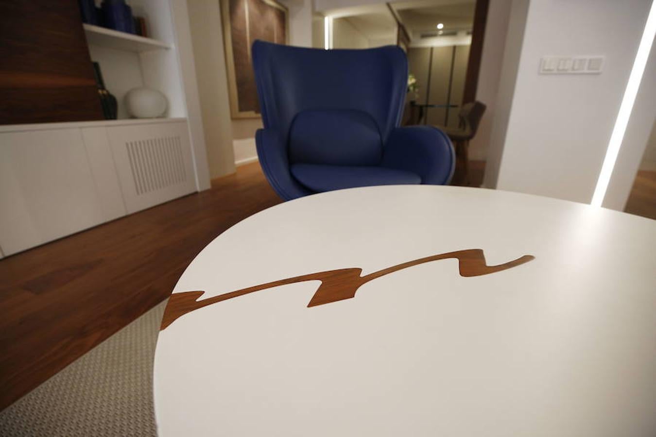 Las peticiones que Mariche Correcher planteó a la diseñadora creativa Carmen Bayarri estaban muy claras: que la casa tuviera muchos armarios, que la cocina y el salón estuviesen unidos pero a la vez se pudieran independizar y que la zona más tranquila de la casa albergara una suerte de suite en la que poder refugiarse después de la jornada de trabajo. Además le pidió que al entrar a la vivienda pudiera ver un ramo de flores. Con estas premisas, hace cuatro años se esbozó el proyecto en esta casa ubicada en una finca con carácter en pleno Ensanche valenciano. Para vestir el suelo escogieron madera de nogal, al igual que en las puertas que dividen las estancias. El resto de las puertas son blancas con las manivelas en negro y van de suelo a techo buscando potenciar la sensación de amplitud. En los baños instalaron porcelánico negro en el suelo que contrasta muy bien con el nogal. Carmen propuso ubicar junto a la entrada una escultura lacada flotante en rojo Ferrari que enmarca el espacio y permite ver el ramo de flores que reposa sobre la mesa del salón nada más entrar, que era uno de los deseos de la propietaria. La iluminación está integrada en la propia arquitectura. En lugar de obviar los pilares se decidió marcarlos de manera interna con filas de luz para ofrecer un ambiente casi escultórico. 