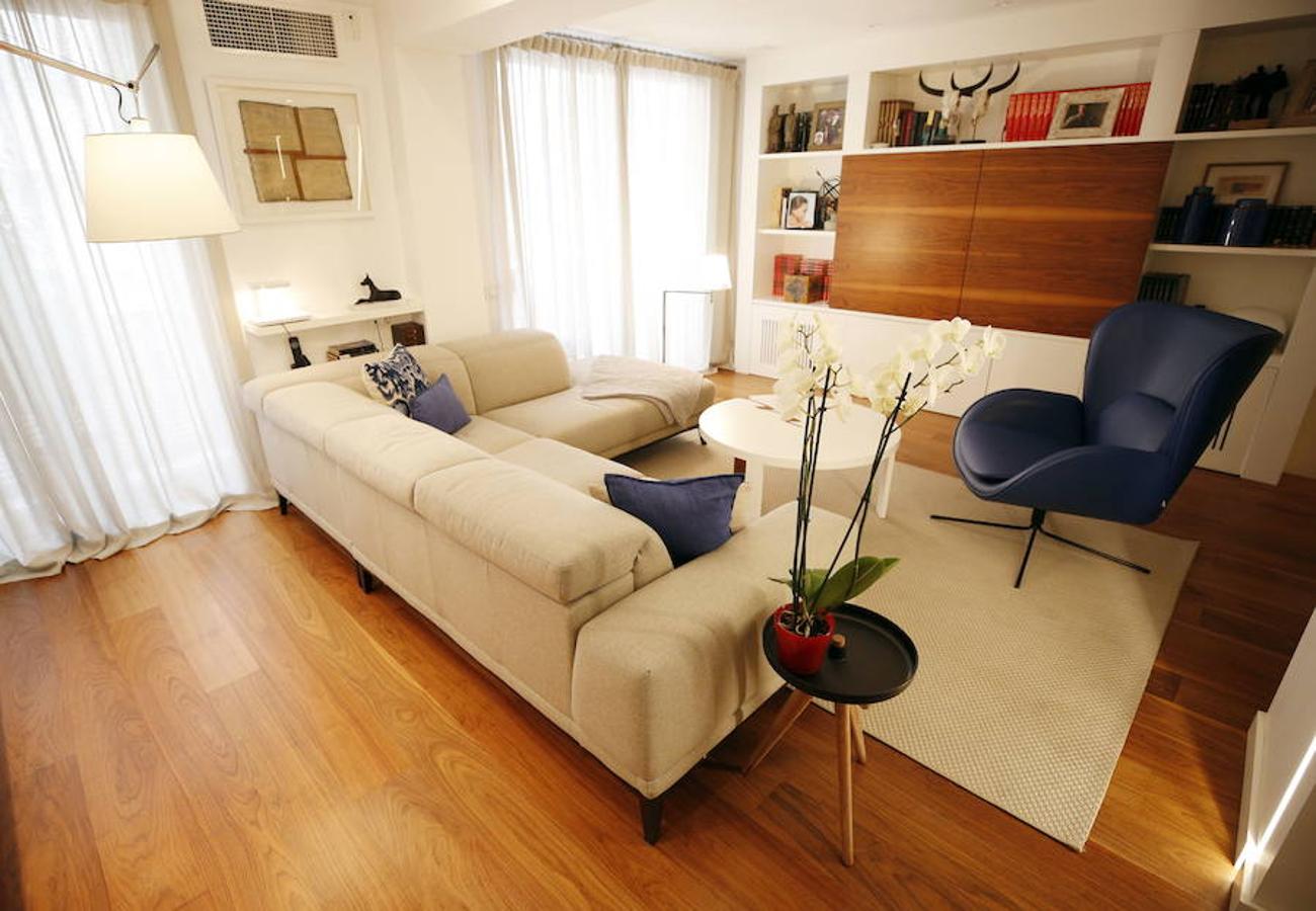 Las peticiones que Mariche Correcher planteó a la diseñadora creativa Carmen Bayarri estaban muy claras: que la casa tuviera muchos armarios, que la cocina y el salón estuviesen unidos pero a la vez se pudieran independizar y que la zona más tranquila de la casa albergara una suerte de suite en la que poder refugiarse después de la jornada de trabajo. Además le pidió que al entrar a la vivienda pudiera ver un ramo de flores. Con estas premisas, hace cuatro años se esbozó el proyecto en esta casa ubicada en una finca con carácter en pleno Ensanche valenciano. Para vestir el suelo escogieron madera de nogal, al igual que en las puertas que dividen las estancias. El resto de las puertas son blancas con las manivelas en negro y van de suelo a techo buscando potenciar la sensación de amplitud. En los baños instalaron porcelánico negro en el suelo que contrasta muy bien con el nogal. Carmen propuso ubicar junto a la entrada una escultura lacada flotante en rojo Ferrari que enmarca el espacio y permite ver el ramo de flores que reposa sobre la mesa del salón nada más entrar, que era uno de los deseos de la propietaria. La iluminación está integrada en la propia arquitectura. En lugar de obviar los pilares se decidió marcarlos de manera interna con filas de luz para ofrecer un ambiente casi escultórico. 