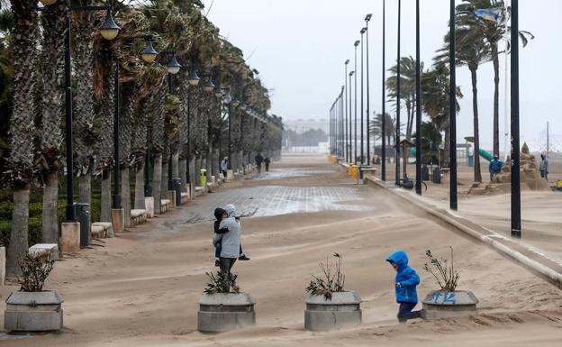 Una mujer cruza el paseo marítimo de Valencia cubierto en parte por la arena que arrastra el fuerte viento. 