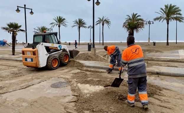 Operarios y máquinas retiran la arena que anega el paseo de la Malvarrosa tras el pasado temporal de lluvia y viento en Valencia.