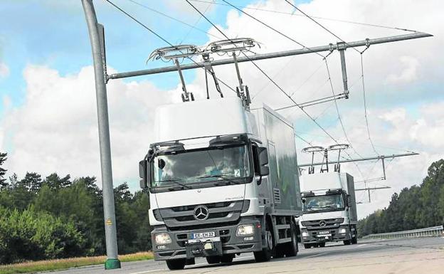 Dos camiones híbridos circulan con sus pantógrafos conectados a la catenaria.