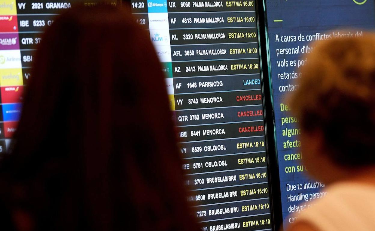 Varias personas se informan en los paneles del aeropuerto del Prat. 