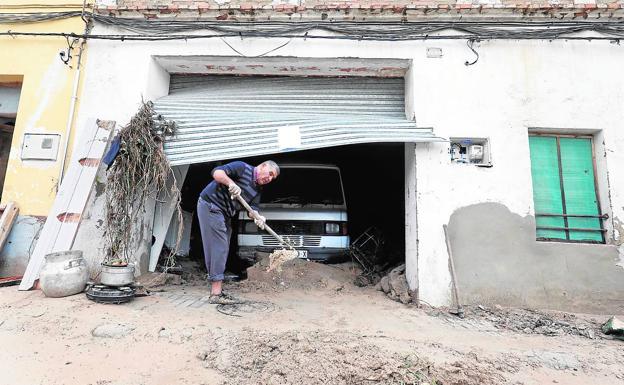 Un vecino afectado por el temporal limpia el fango en la puerta de su casa.