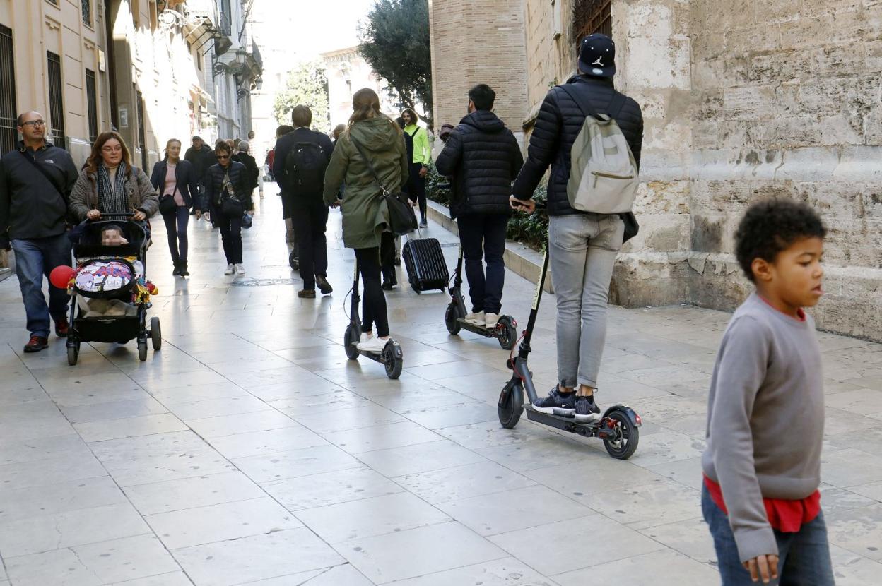 Usuarios de patinete circulan por la calle del Micalet, peatonal. 