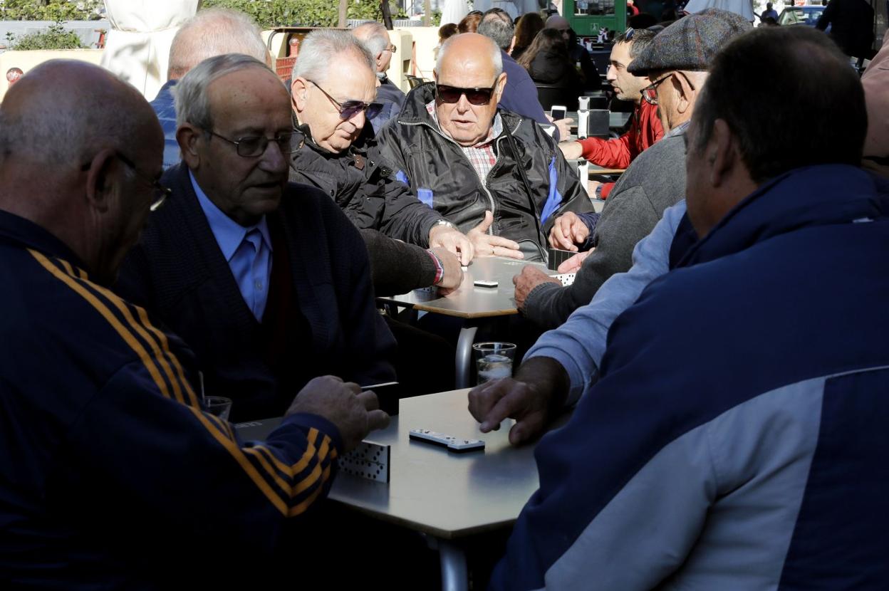 Varios grupos de jubilados juegan partidas de dominó en la terraza de un bar. 