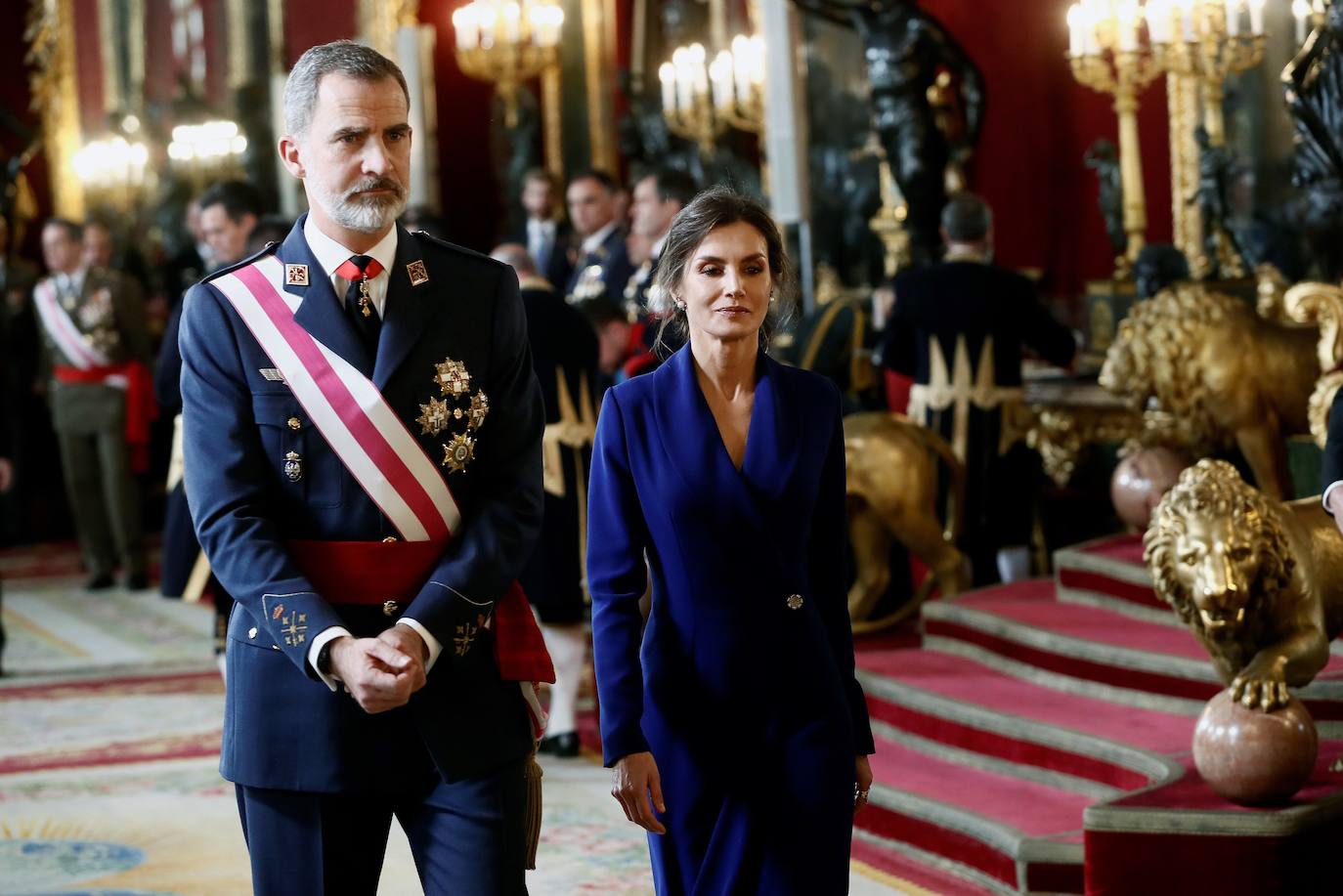 Felipe VI, acompañado por la Reina Letizia, ha presidido este lunes la ceremonia de la Pascua Militar en el Palacio Real. Para la ocasión, Doña Letizia ha elegido un elegante vestido de estilo esmoquin en azul intenso. La Reina ha combinado el diseño, largo hasta los pies, con unos zapatos stilettos en color negro y un peinado recogido acabado en un moño bajo.