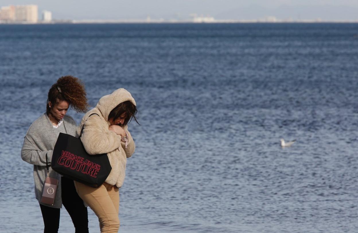 Dos mujeres se protegen del viento, ayer, en la playa de la Malvarrosa. 