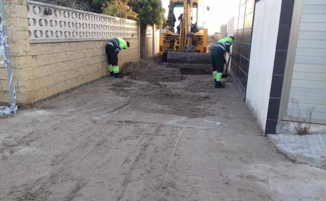 Operarios municipales retiran los montones de arena que el mar arrastró hasta las calles de Marenys