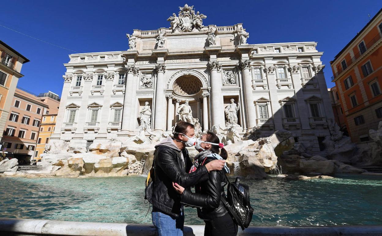 Una pareja se besa ante la Fontana di Trevi de Roma con mascarillas. 