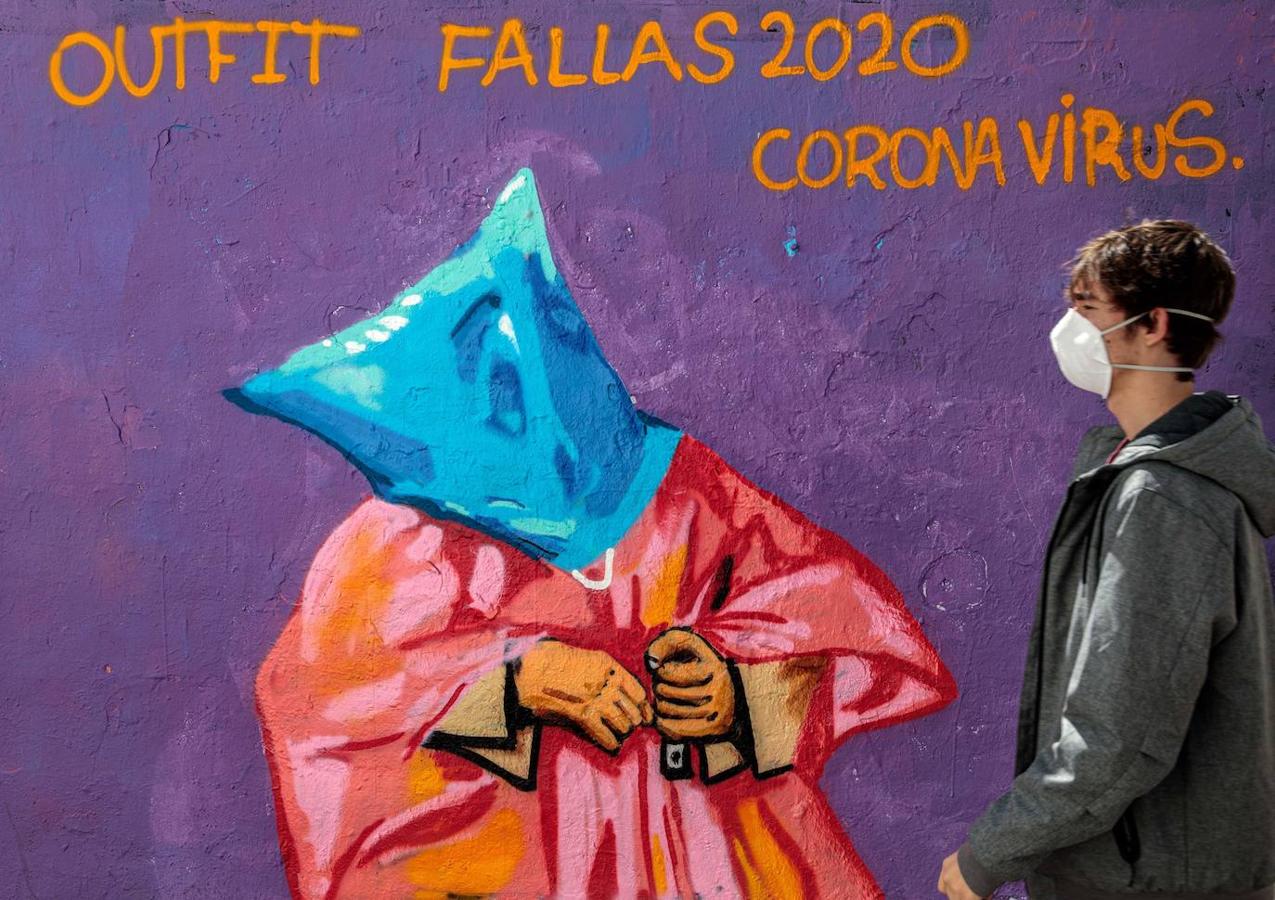 Una persona con mascarilla pasa frente a una pintura mural en referencia a las Fallas y el coronavirus. 