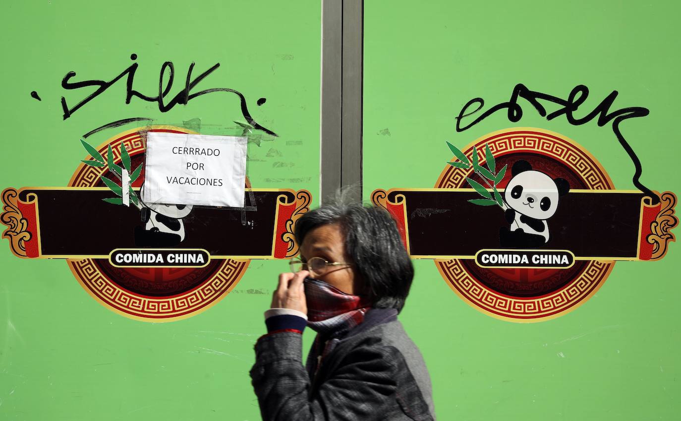 Una mujer con mascarilla pasa ante una tienda regentada por ciudadanos chinos en el centro de Valencia, en el entorno de la calle Bailén, donde la mayoría de los negocios chinos ha utilizado el 'Cerrado por vacaciones' para justificar el cierre el miedo al coronavirus. 