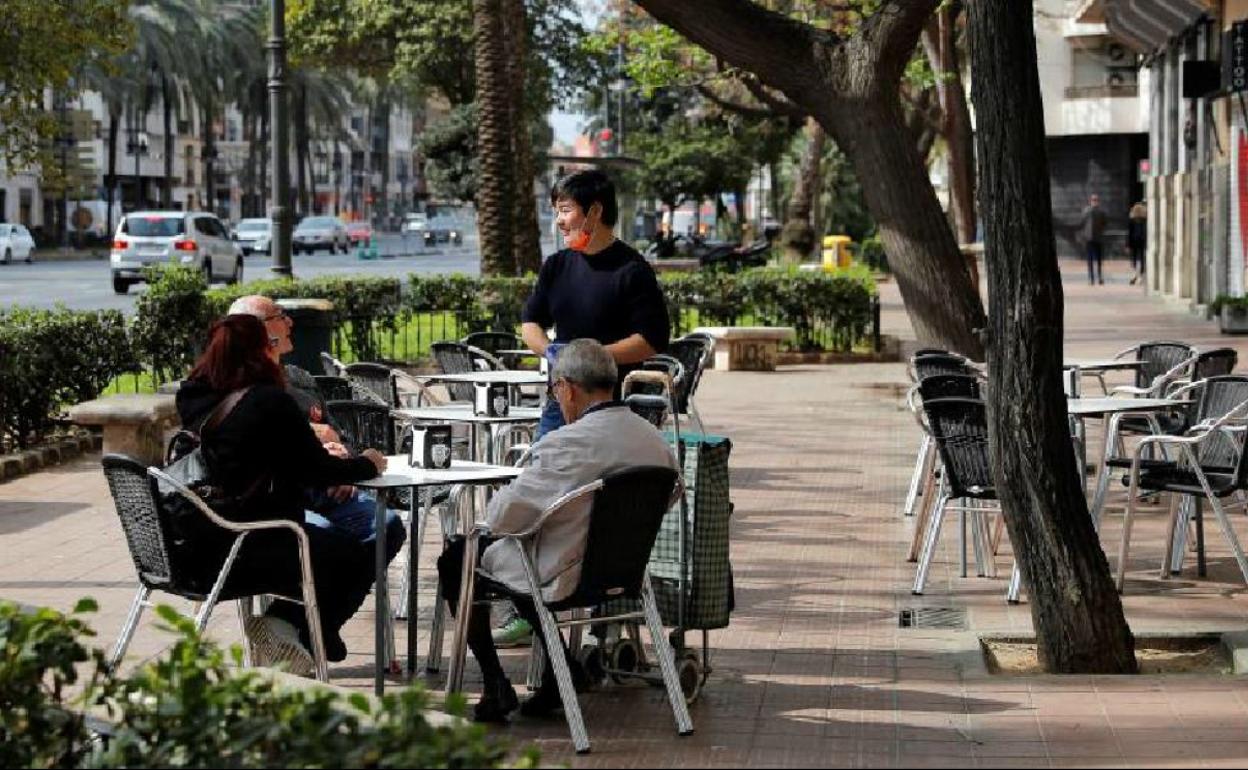 Un camarero, protegido con guantes y mascarilla, atiende a unos clientes en una terraza de Valencia. 