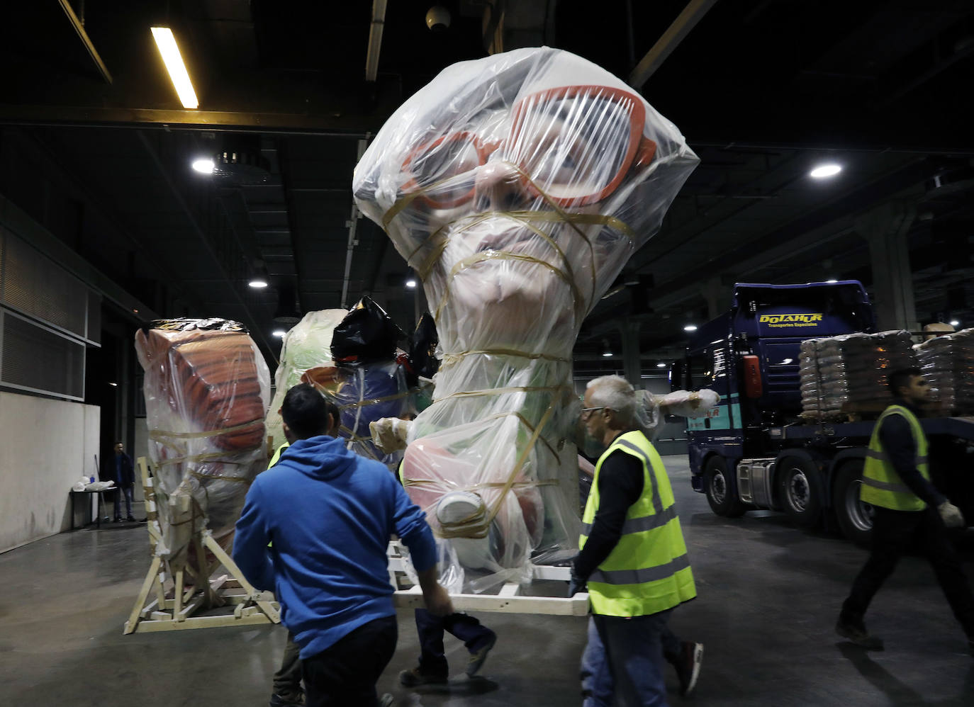 Las instalaciones de Feria Valencia han empezado a acoger, a última hora de este viernes, las piezas de distintas fallas de València que no habían sido aún plantadas en las calles y que permanecerán ahora resguardadas hasta el próximo mes de julio. Piezas de gran tamaño y de todos los colores y formas posibles han ido entrando paulatinamente a bordo de varios camiones en una de las grandes naves de Feria Valencia habilitadas expresamente para esta medida de urgencia, adoptada esta semana tras la decisión del aplazamiento de las Fallas ante la pandemia del coronavirus. Está previsto que distintas comisiones falleras lleven allí sus piezas más grandes hasta julio, cuando volverán a tomar las calles para la Plantà definitiva de los monumentos, que arderán el 19 de julio.