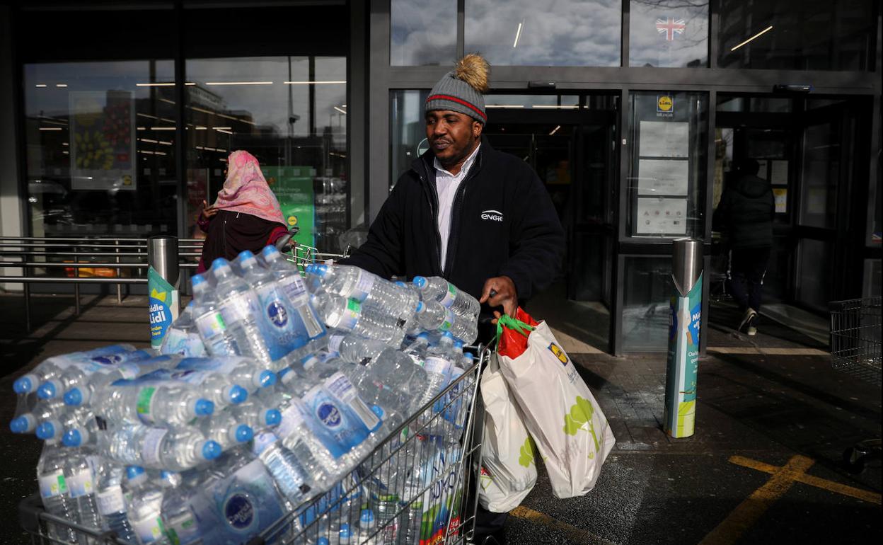 Un hombre sale con un carro repleto de agua embotellada de un Lidl en Londres.