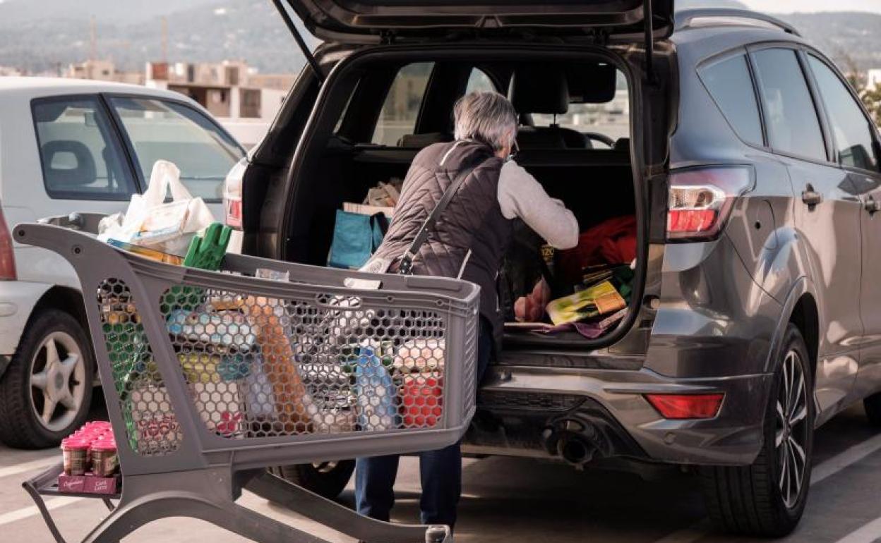 Una mujer carga en el coche la cesta de la compra. 