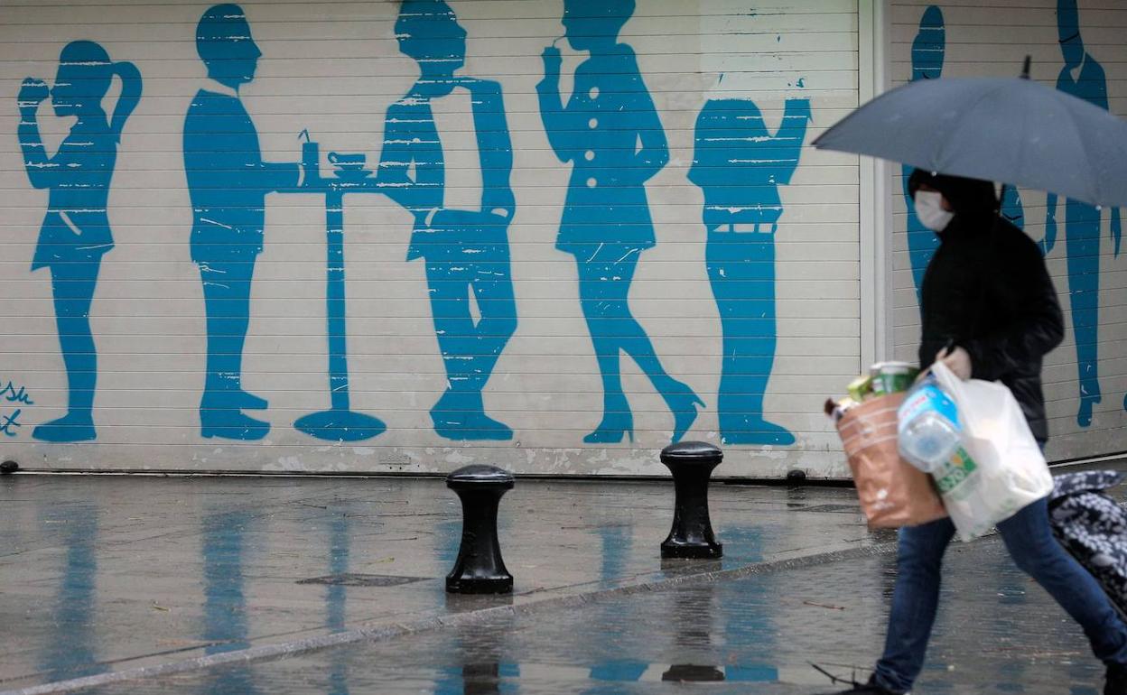 Una persona con bolsas y mascarilla en un día lluvioso en Valencia. 