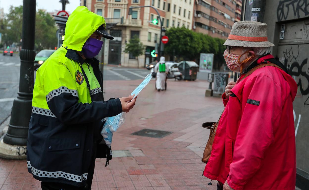 Un agente de policía local de Valencia entrega mascarillas a untranseúnte. 