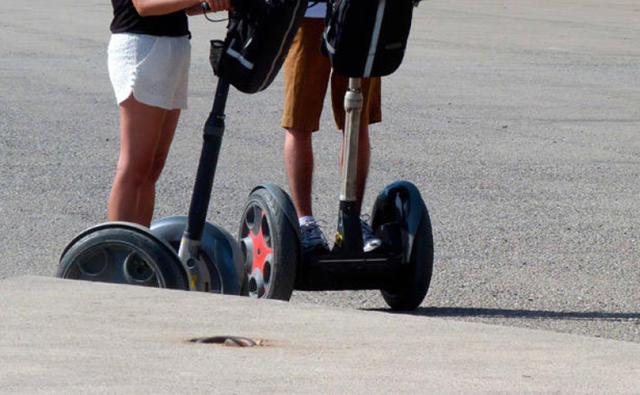 Dos usuarios de patinete eléctrico circulan por una vía pública.