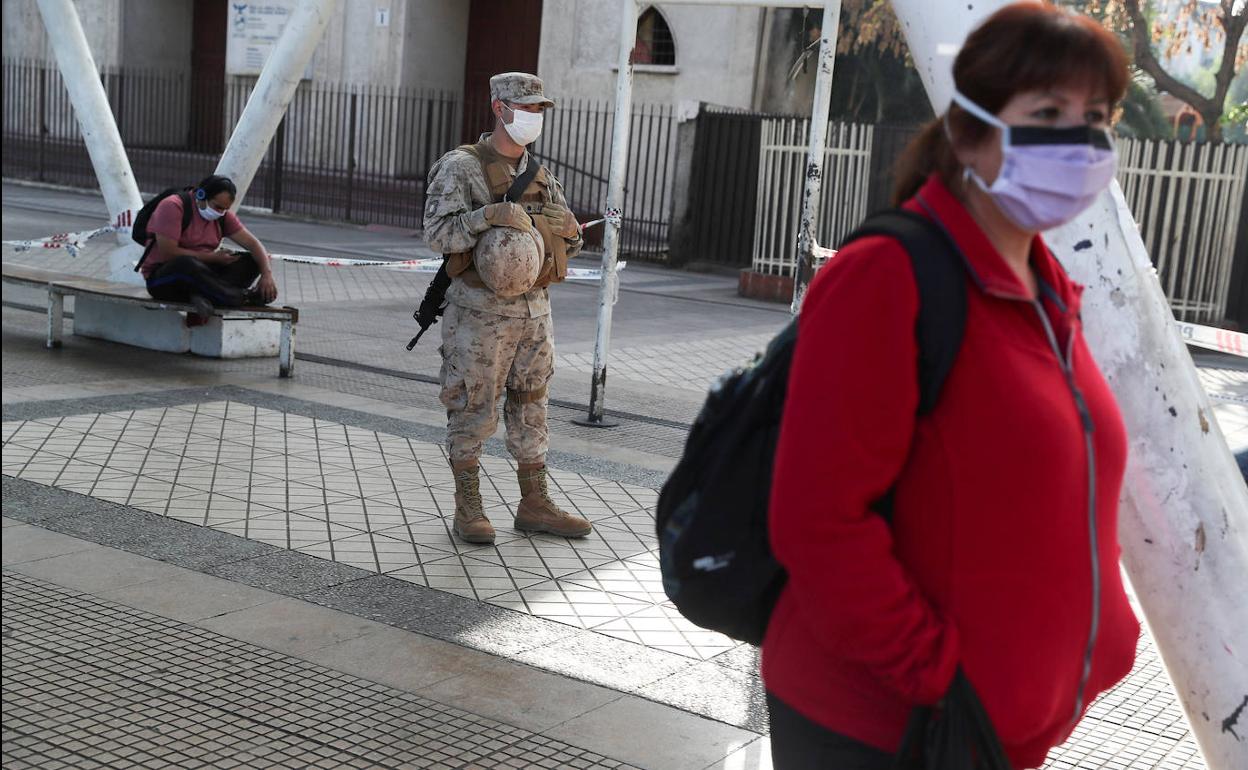 Una mujer pasea con mascarilla por Santiago de Chile bajo la atenta mirada de un militar.