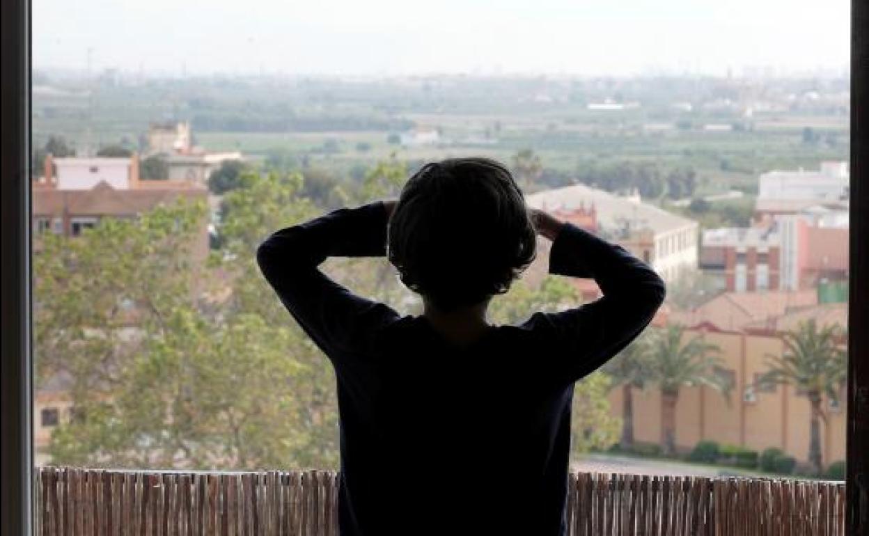 Un niño mira por la ventana de su casa. 